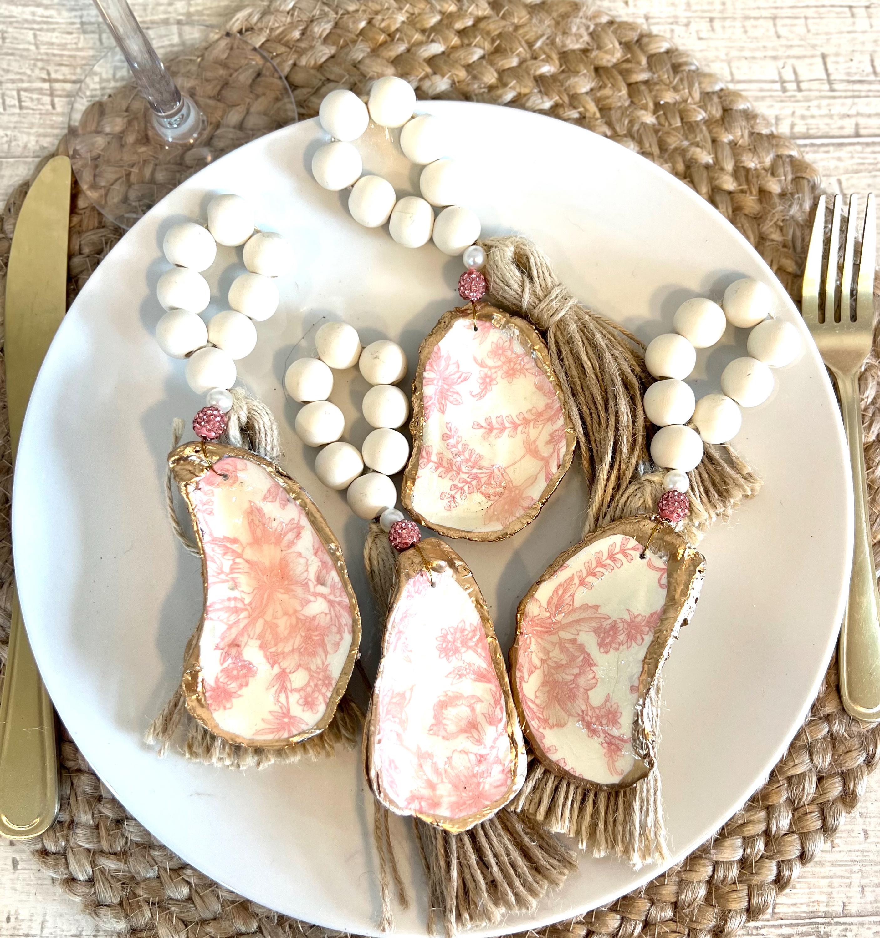 pink toile design oyster shell napkin rings with wood beads and gold leaf rim on a white plate with a white flower