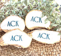 ACK the abbreviation for Nantucket in navy blue capital letters on a white background on large oyster shell dish favors for weddings or beach parties with a gold leaf painted trim